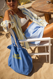 Chemise rayée en gaze portée par une femme, assise, sac bleu, chaise blanche