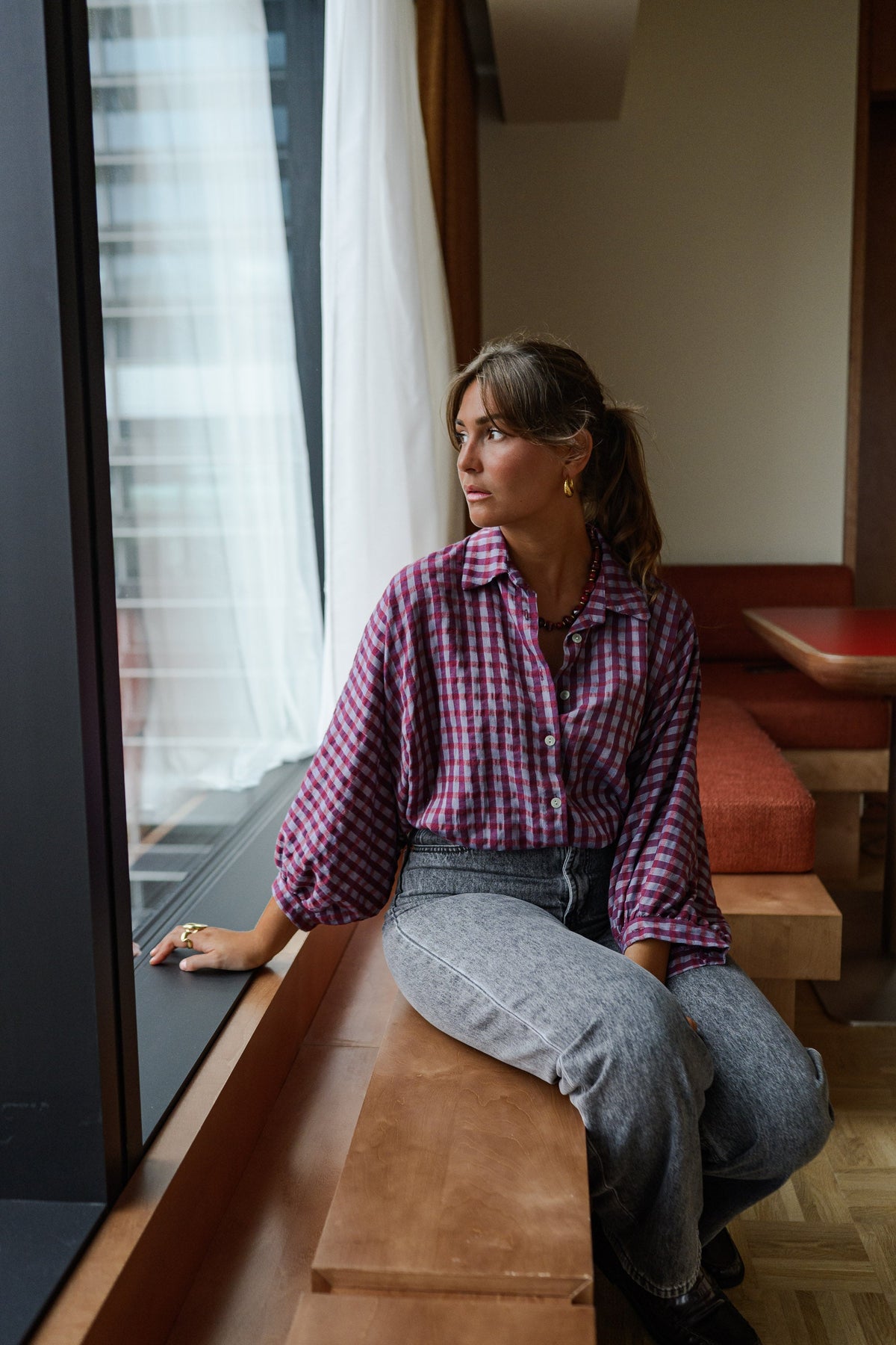 Chemise à carreaux col chemise portée par une femme, assise, sur un banc près de la fenêtre
