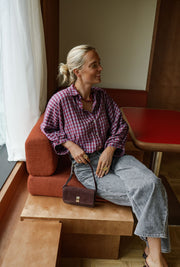 Chemise à carreaux col chemise portée par une femme, assise, sur une banquette, sac à main