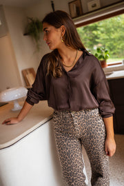Chemise satinée fluide chocolat portée par une femme, assise, îlot de cuisine, pantalon léopard