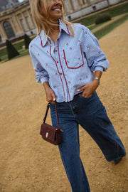 Chemise rayée brodée à cerises portée par une femme, vue de trois-quarts, sac bordeaux, jean large