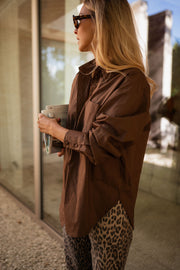 Chemise manches longues loose chocolat portée par une femme, vue de profil, vitre, pantalon léopard