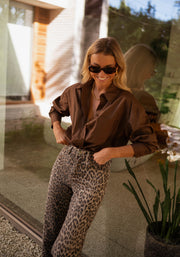 Chemise manches longues loose chocolat portée par une femme, vue de face, lunettes, pantalon léopard
