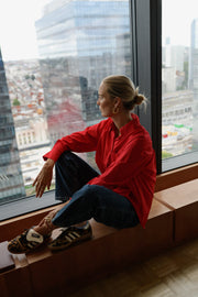 Chemise ample à manches longues rouge portée par une femme, assise, vue de face