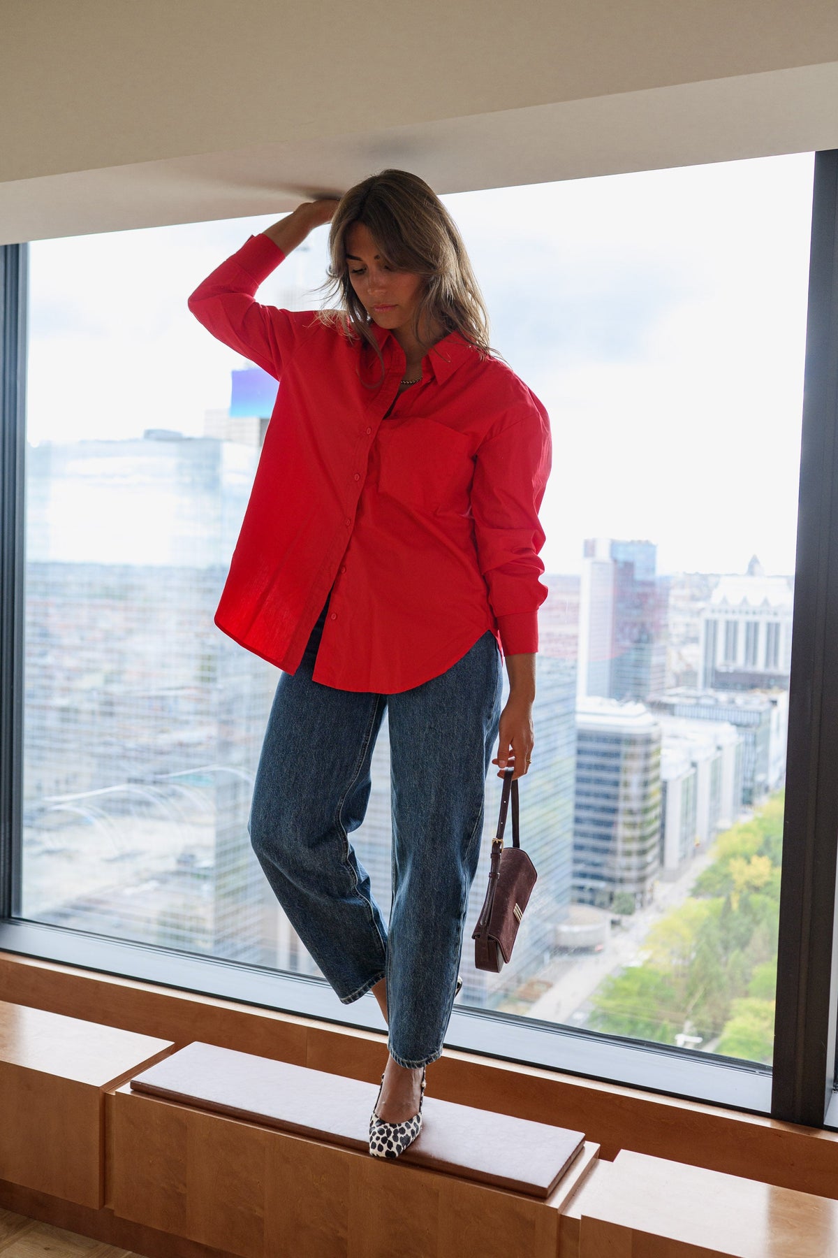 Chemise ample à manches longues rouge portée par une femme, silhouette entière, près d'une fenêtre