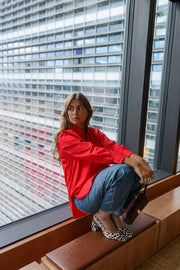 Chemise ample à manches longues rouge portée par une femme, assise, sur un banc