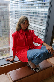 Chemise ample à manches longues rouge portée par une femme, assise, vue de profil