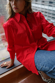 Chemise ample à manches longues rouge portée par une femme, assise, sur le rebord, vue rapprochée