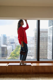 Chemise ample à manches longues rouge portée par une femme, vue de dos, bras levés, silhouette entière