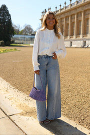 Chemise transparente à brandebourgs portée par une femme, silhouette entière, jean, sac violet à la main