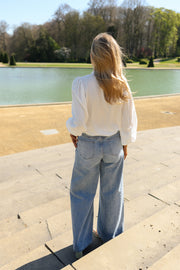 Chemise transparente à brandebourgs portée par une femme, vue de dos, jean, devant un bassin