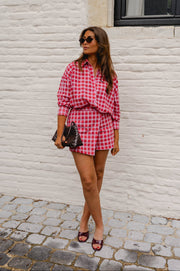 Chemise à carreaux brillante portée par une femme, silhouette entière, sac noir à la main, short assorti