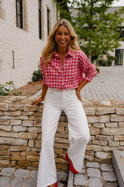 Chemise à carreaux brillante portée par une femme, vue de trois-quarts, pantalon blanc, sur un muret