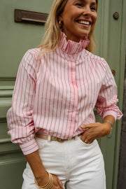 Chemise rayée à col victorien portée par une femme, vue rapprochée, porte verte, pantalon blanc