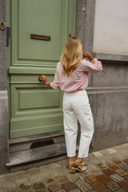 Chemise rayée à col victorien portée par une femme, vue de dos, porte verte, pantalon blanc