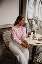 Chemise rayée à col victorien portée par une femme, assise, à une table, de profil