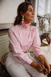 Chemise rayée à col victorien portée par une femme, assise, à une table, boucles d'oreilles