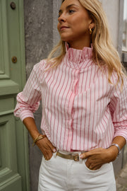Chemise rayée à col victorien portée par une femme, vue rapprochée, mains dans les poches, porte verte