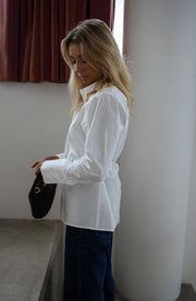 Chemise cintrée à nouer blanche portée par une femme, vue de trois-quarts, colonne blanche, mains dans les poches