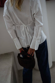 Chemise cintrée à nouer blanche portée par une femme, vue de dos, nœud dans le dos, sac noir