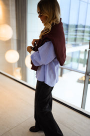 Chemise ample à carreaux portée par une femme, vue de trois-quarts, pull bordeaux sur les épaules, cheveux blonds