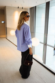 Chemise ample à carreaux portée par une femme, vue de dos, baie vitrée, sac noir