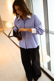 Chemise ample à carreaux portée par une femme, vue de trois-quarts, baie vitrée, sac noir