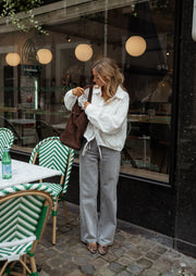 Chemise courte à poches blanche portée par une femme, vue de face, chaises vertes, jean gris