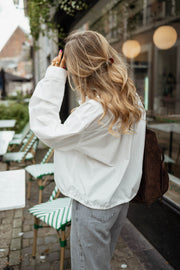 Chemise courte à poches blanche portée par une femme, vue de dos, cheveux blonds, sac