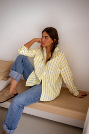 Chemise rayée coupe loose jaune portée par une femme, assise, banc en bois, jean retroussé