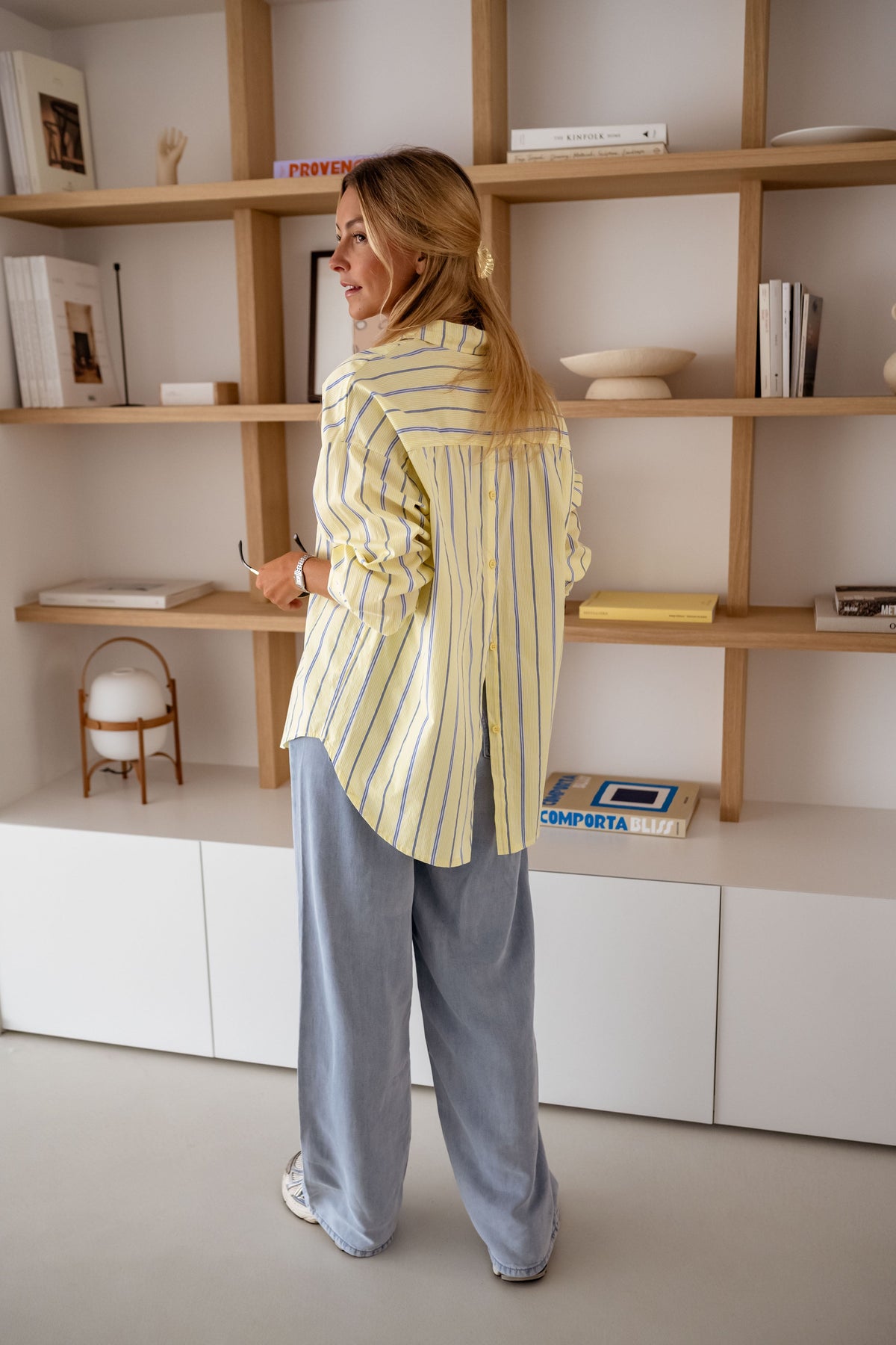 Chemise rayée coupe loose jaune portée par une femme, vue de dos, étagères en bois, jean clair