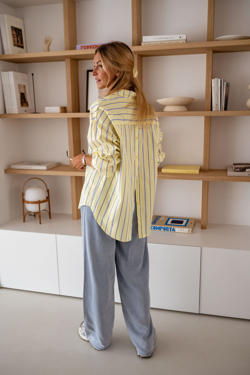 Chemise rayée coupe loose jaune portée par une femme, vue de dos, étagères en bois, jean clair