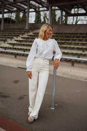 Chemise brodée col claudine blanche portée par une femme, vue de face, gradins, pantalon blanc