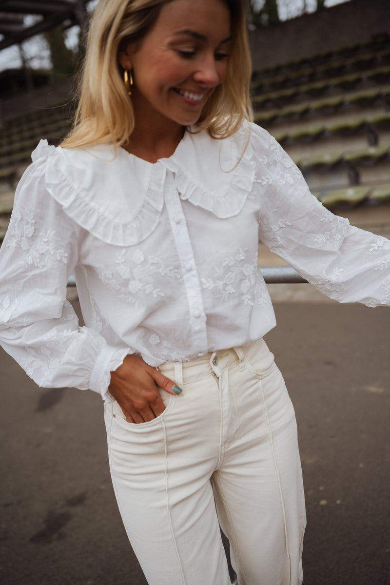 Chemise brodée col claudine blanche portée par une femme, vue rapprochée, col à volants, sourire