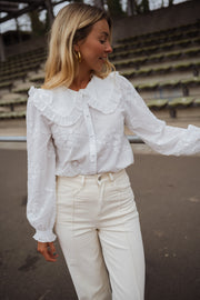 Chemise brodée col claudine blanche portée par une femme, vue de trois-quarts, gradins, pantalon blanc