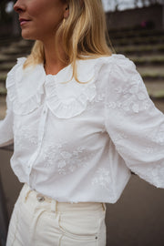 Chemise brodée col claudine blanche portée par une femme, vue rapprochée, volants au col, cheveux blonds
