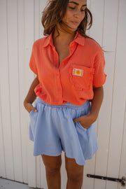 Chemise fluide à plumetis corail portée par une femme, silhouette entière, short bleu clair, cabines
