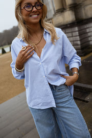 Chemise rayée dos cœur ouvert portée par une femme, vue de trois-quarts, lunettes de soleil, collier