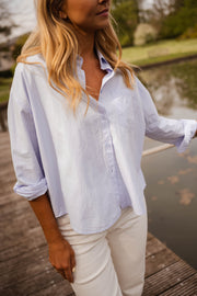 Chemise ample à rayures portée par une femme, vue rapprochée, manche relevée, pantalon blanc