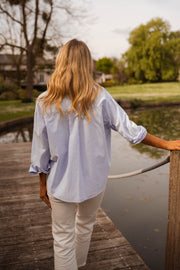 Chemise ample à rayures portée par une femme, vue de dos, ponton en bois, cheveux blonds
