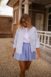 Chemise ample à rayures portée par une femme, vue de face, véranda en bois, short bleu