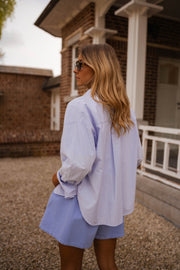 Chemise ample à rayures portée par une femme, vue de trois-quarts, véranda en bois, short bleu