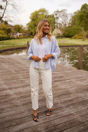 Chemise ample à rayures portée par une femme, vue de face, ponton en bois, pantalon blanc