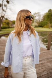 Chemise ample à rayures portée par une femme, vue de face, lunettes de soleil, ponton en bois