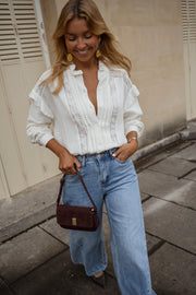 Chemise en gaze brodée portée par une femme, vue de face, allée dallée, sac bordeaux