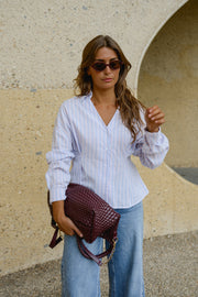 Chemise cintrée manches longues portée par une femme, vue de trois-quarts, lunettes de soleil, sac bordeaux à l'épaule