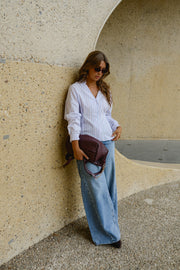 Chemise cintrée manches longues portée par une femme, silhouette entière, sac bordeaux, devant un mur courbe