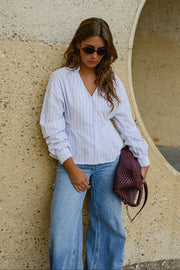 Chemise cintrée manches longues portée par une femme, vue rapprochée, lunettes de soleil, sac à l'épaule