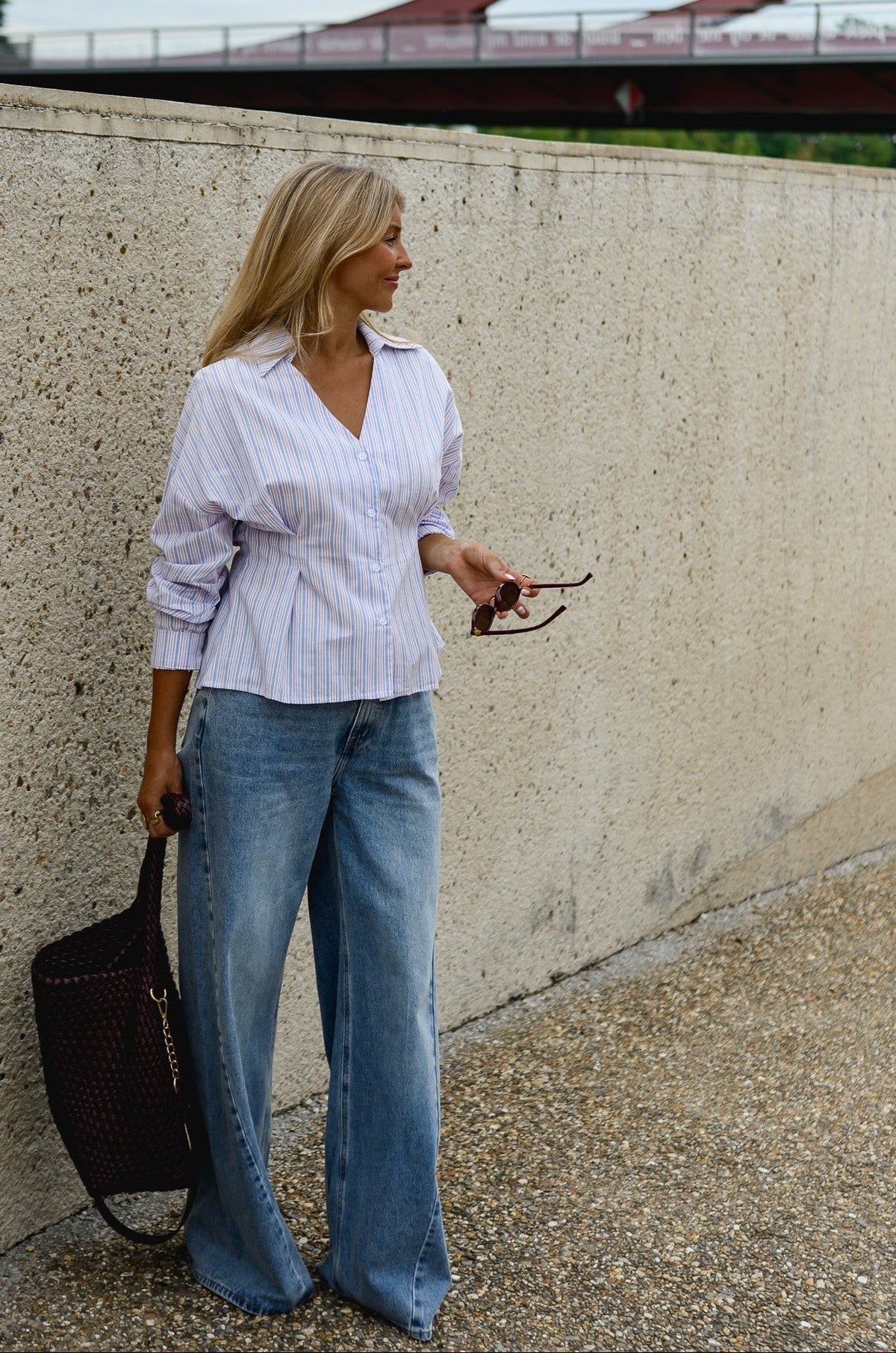 Chemise cintrée manches longues portée par une femme, vue de trois-quarts, lunettes à la main