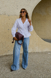Chemise cintrée manches longues portée par une femme, vue de trois-quarts, lunettes de soleil, sac bordeaux